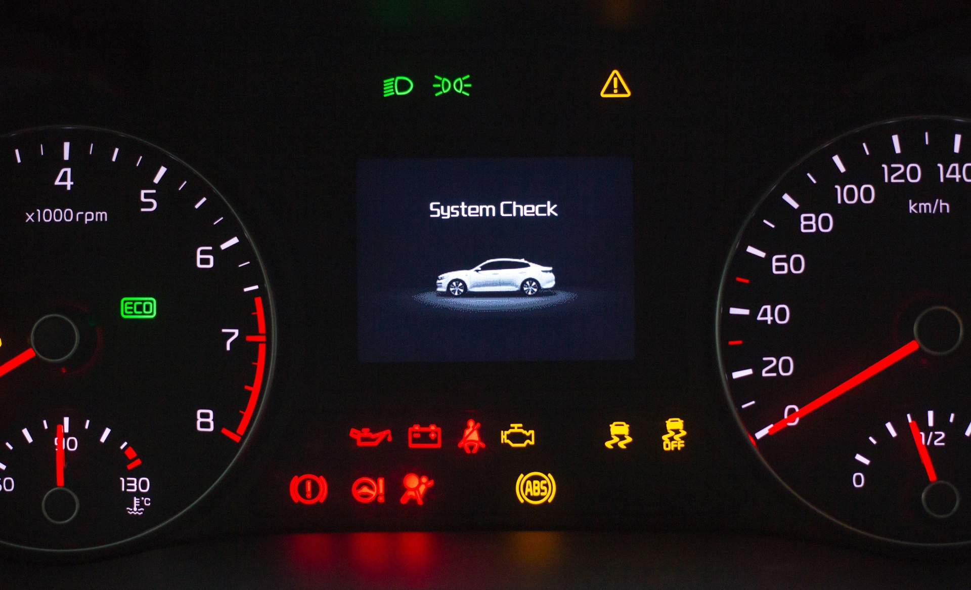 Car dashboard instrument cluster with illuminated warning lights including check engine, brake system, tire pressure, and fuel indicator, shown across the speedometer and tachometer displays.